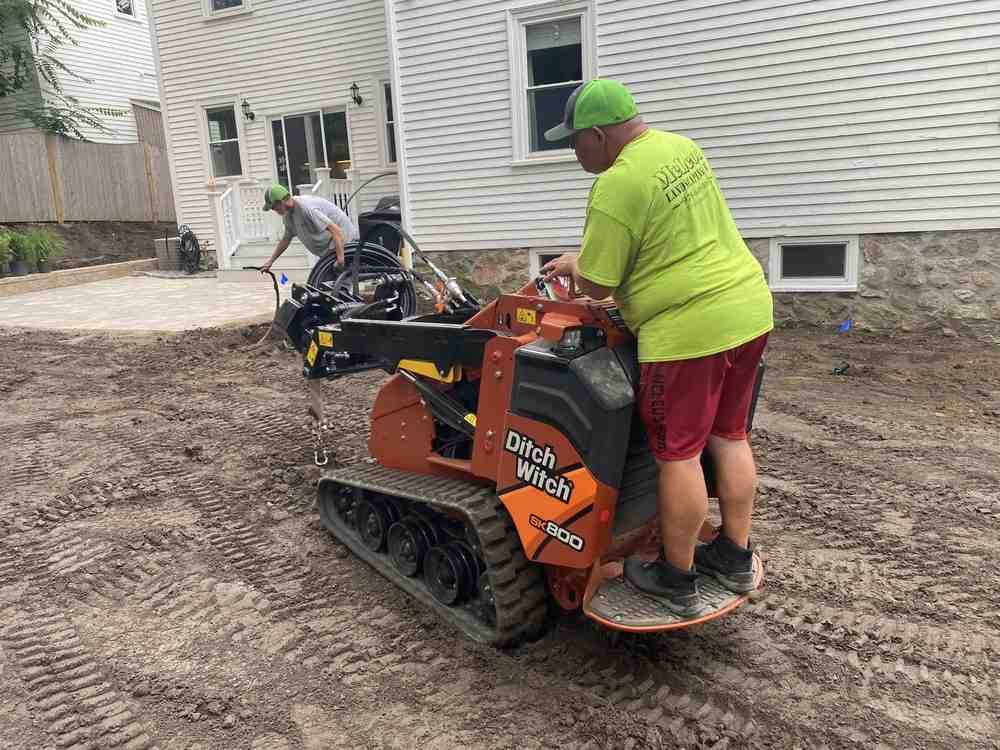 Multi-level patio with integrated fire pit surrounded by natural stone seating walls and landscape lighting - Custom Patio Builder